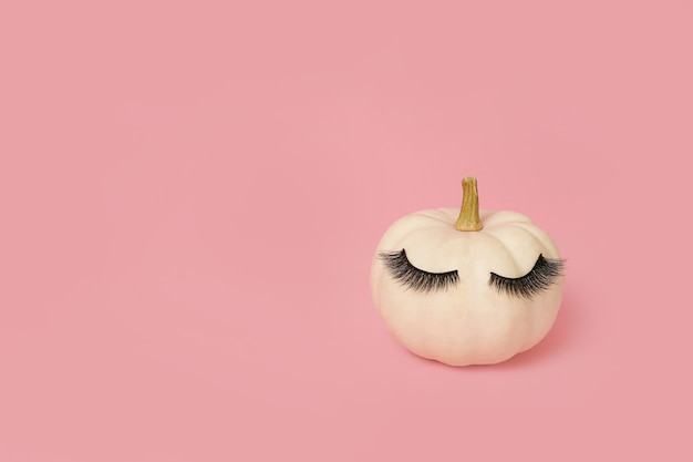 Zucca bianca di Halloween con ciglia truccate. Fondo di rosa di concetto minimo di stagione di festa.