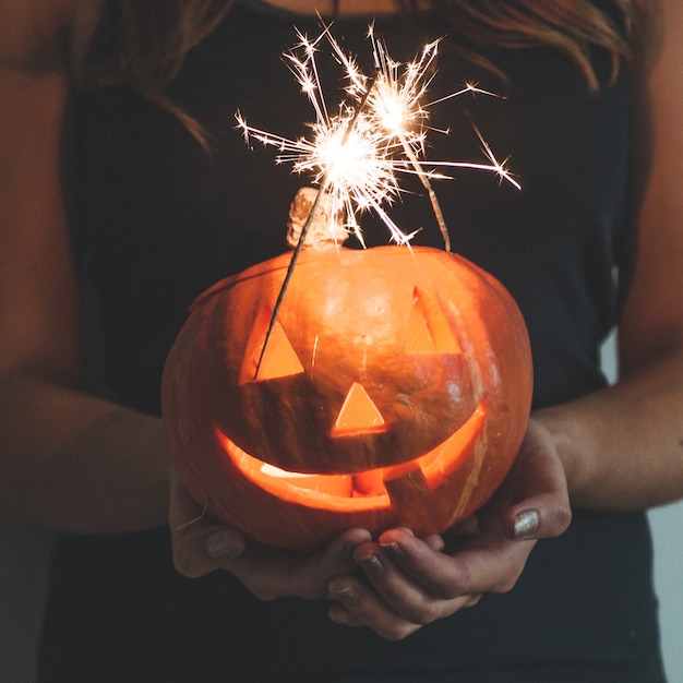 Zucca di Halloween nelle mani di una ragazza con le luci del Bengala. Concetto di vacanza di Halloween. Bella donna con le zucche.