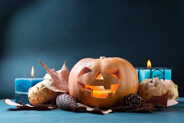 Zucca di Halloween sull'azzurro con le candele e foglie e pigne di autunno.