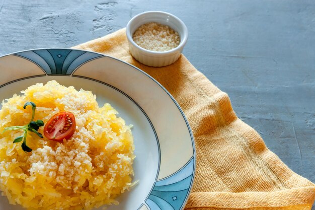 Zucca di spaghetti biologici cucinati freschi Cucurbita pepo vegetale su sfondo grigio con formaggio grattugiato