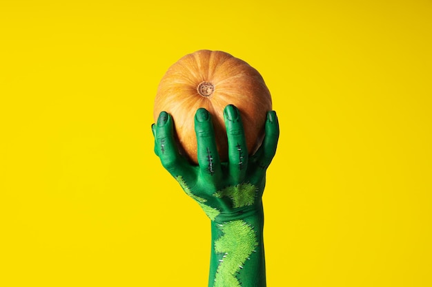 Zucca in mano femminile verde su sfondo giallo da vicino