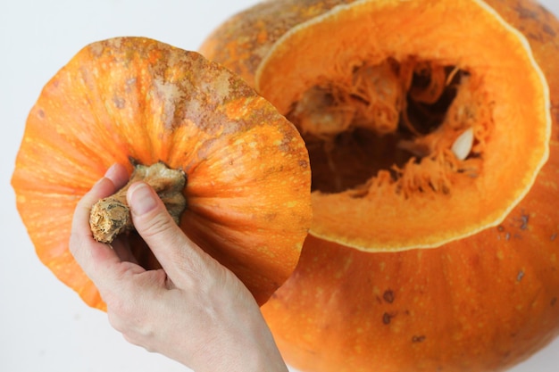 Zucca intera dopo diversi minuti in forno e mani di donna che tengono la parte superiore della zucca tagliata sullo sfondo bianco. Concetto come tagliare la zucca con la buccia dura