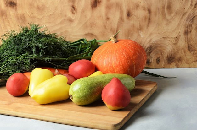 Zucca, pomodori, cipolle, zucchine, peperoni, carote e aneto su uno sfondo di legno.