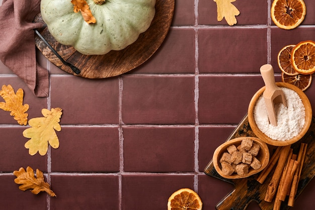 Zucca. Sfondo di cibo autunnale con cannella, noci e spezie stagionali su vecchie piastrelle di ceramica sfondo. Cucinare zucca o torta di mele e biscotti per il Ringraziamento e le vacanze autunnali. Vista dall'alto.