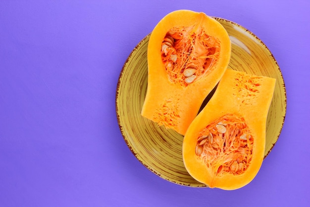 Zucca succosa arancione metà su un piatto bianco su sfondo viola Vista dall'alto Concetto di cibo vegetariano Primo piano