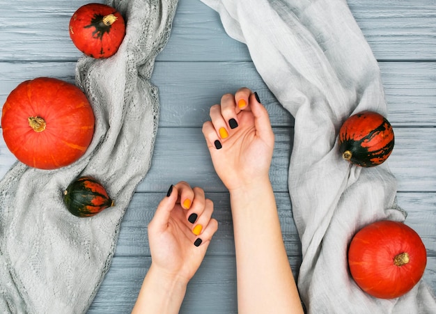 Zucche arancioni su sfondo grigio Mani femminili con manicure autunnale su sfondo grigio con zucche arancioni Vista dall'alto