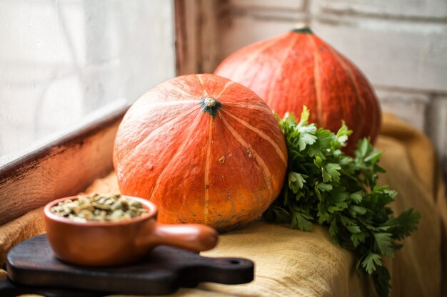 Zucche mature semi di girasole di zucca e mazzetto di prezzemolo su un tovagliolo di lino giallo sul davanzale di una finestra