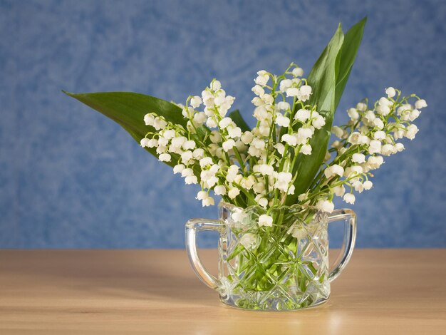 Zuccheriera di cristallo con Lilly of the Valley su una credenza, carta da parati blu su sfondo