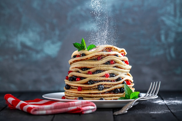 Zucchero a velo di versamento su pancake al forno fatti in casa con frutti di bosco freschi e menta per uno spuntino delizioso