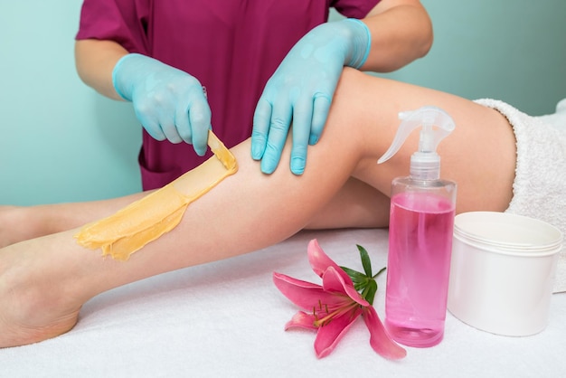 Zucchero delle gambe Un'estetista fa una depilazione in pasta di zucchero delle gambe di una donna in un salone di bellezza Cosmetologia estetica femminile Applicare la pasta di zucchero con una spatola di legno