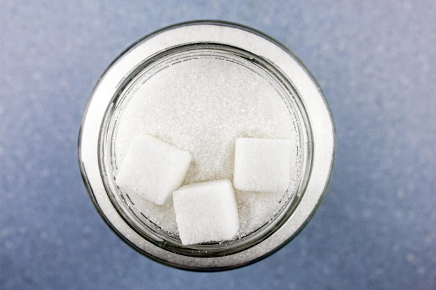 Zucchero in un barattolo di vetro Pezzi di zollette di zucchero e briciole di zucchero Concetto di zucchero su una vista da tavolo blu