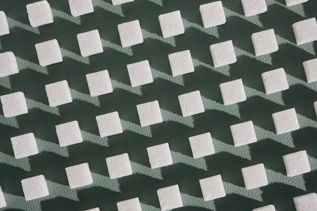 Zucchero raffinato su sfondo verde. Cubetti di zucchero dolce e bianco in forma geometrica. Ombre dure.