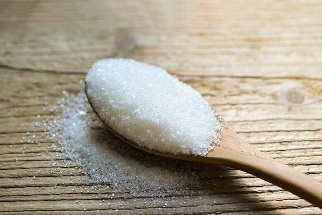 Zucchero sul cucchiaio e fondo in legno zucchero bianco per alimenti e dolci caramella da dessert mucchio di granulato cristallino di zucchero dolce