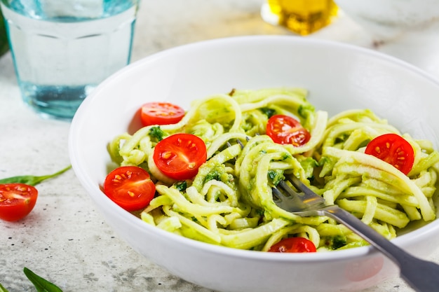 Zucchine al pesto, avocado e pomodori in zolla bianca. Concetto di cibo vegan crudo.