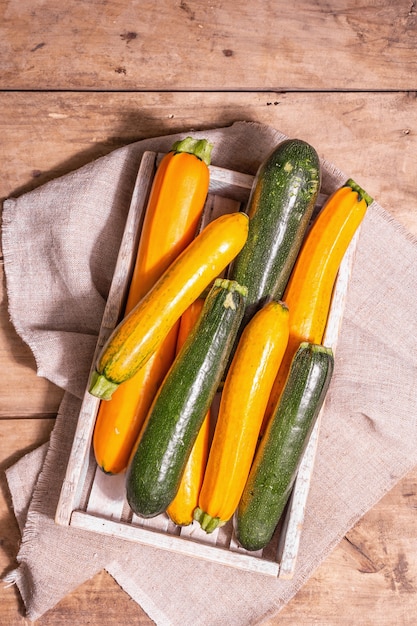 Zucchine fresche assortite. Verdure mature raccolte in una scatola di legno. Tavolo con tavole vintage, vista dall'alto