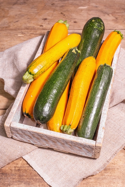 Zucchine fresche assortite. Verdure mature raccolte in una scatola di legno. Tavolo con tavole vintage, vista dall'alto