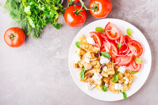 Zucchine fritte con formaggio feta, pomodori, erbe e cipolle su un piatto