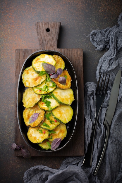 Zucchine fritte con peperoncino, basilico e prezzemolo in una padella in ghisa su una vecchia superficie scura