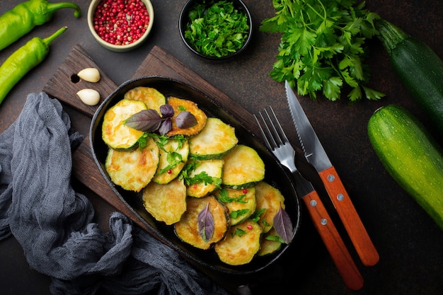 Zucchine fritte con peperoncino, basilico e prezzemolo in una padella in ghisa su una vecchia superficie scura