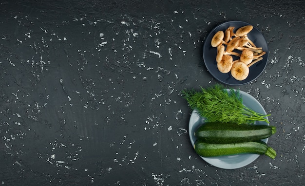 Zucchine, funghi, spezie ed erbe fresche su un bordo nero nella vista superiore con lo spazio della copia