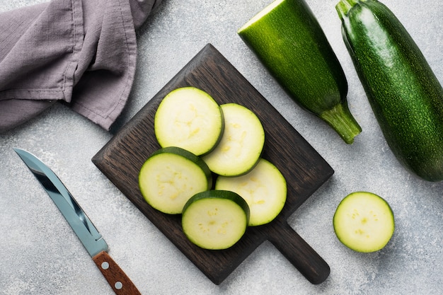 Zucchine verdi fresche tagliate a fette su un tagliere. Sfondo grigio cemento. Avvicinamento.