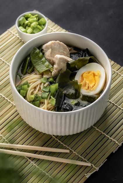 Zuppa asiatica di ramen con pollo e pasta all'uovo con aggiunta di cipolle fresche su una superficie scura di copyspace per menu e articoli con ricette