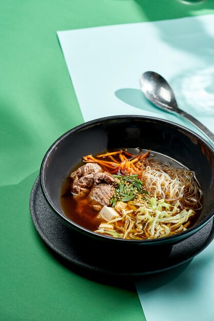 Zuppa asiatica pho bo con manzo, tofu, noodles e cipolle in un piatto di sfondi luminosi. Messa a fuoco selettiva, luce dura