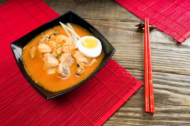 Zuppa con gamberi in ciotola con pomodori ed erbe sul tavolo di legno.