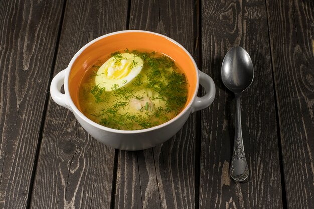 Zuppa con noodles, pollo, uova e aneto su uno sfondo di legno scuro in un piatto con un cucchiaio