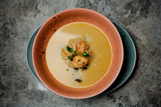 Zuppa cremosa di gamberi ed erbe aromatiche, in un piatto arancione, si erge su un fondo di marmo.