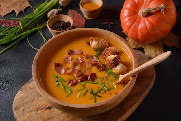 Zuppa cremosa di zucca e patate dolci (batata) con pancetta su sfondo scuro. Una ciotola di zuppa con crostini di pane fatti in casa ed erbe aromatiche con decorazioni autunnali.