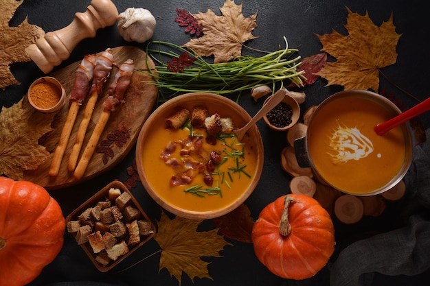 Zuppa cremosa di zucca e patate dolci (batata) con pancetta su sfondo scuro. Una ciotola di zuppa con crostini di pane fatti in casa ed erbe aromatiche con decorazioni autunnali.