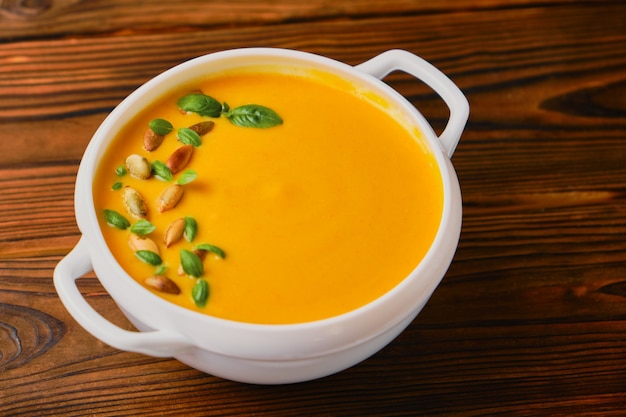 Zuppa cremosa di zucca in una ciotola con semi e basilico su fondo di legno. Ringraziamento, zuppa autunnale