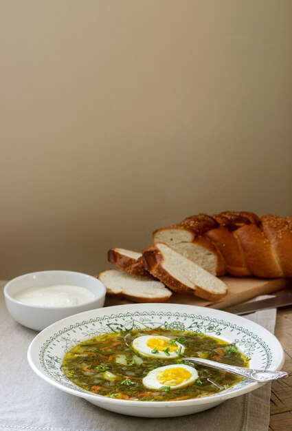 Zuppa di acetosa vegetariana con uovo, servita con panna acida e pane. Stile rustico.