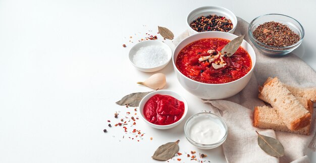 Zuppa di barbabietola rossa, aglio e panna acida su fondo di pane e alloro, borscht su fondo chiaro. Acqua di lato, panorama.