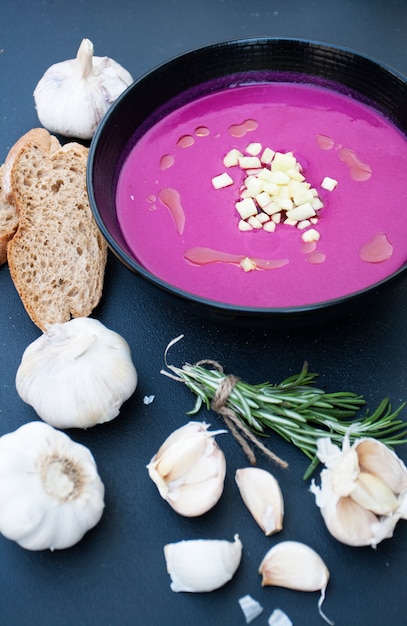 Zuppa di barbabietole con aglio e rosmarino e baguette di segale su una superficie di legno nera