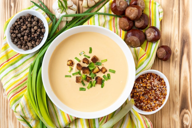 Zuppa di castagne su un tavolo in legno chiaro con condimenti. Vista dall'alto.