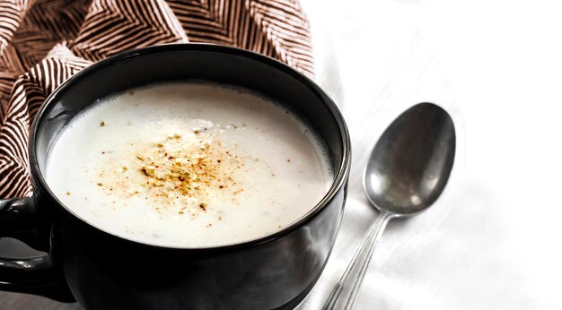 Zuppa di cavolfiore (Creme du Barry) in una ciotola nera su sfondo bianco con un panno. Copia spazio