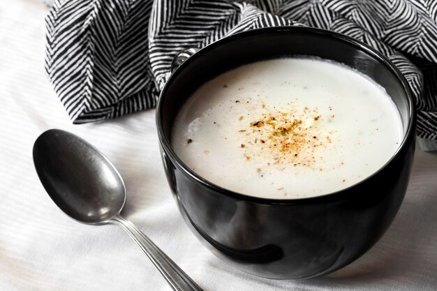 Zuppa di cavolfiore in una ciotola nera su superficie bianca con panno bianco e nero