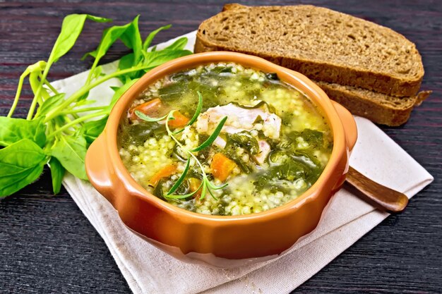 Zuppa di costolette di maiale con couscous e spinaci in una ciotola di argilla su tovagliolo, pane su fondo di legno scuro