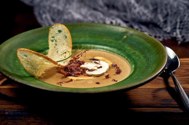 Zuppa di crema di funghi con crostino e panna in un piatto verde. Primo piano, fuoco selettivo