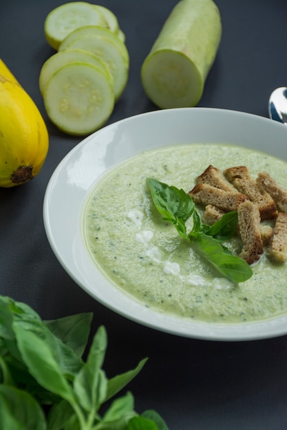 Zuppa di crema di purè di patate con zucchine e basilico e cracker su uno sfondo scuro.