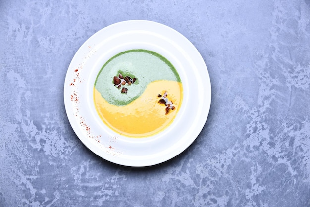 Zuppa di crema di spinaci e zucca su sfondo grigio. Purea di colore verde e giallo nel segno yin yang con pezzi di pancetta in piatto bianco. Decorazione zuppa giapponese. Concetto di cucina tradizionale