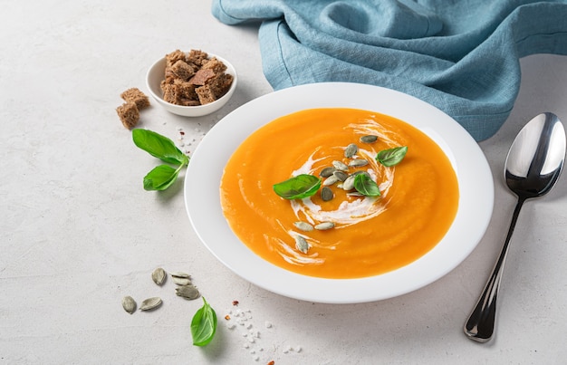 Zuppa di crema di zucca autunnale con basilico e panna su sfondo grigio Spazio vista laterale per la copia