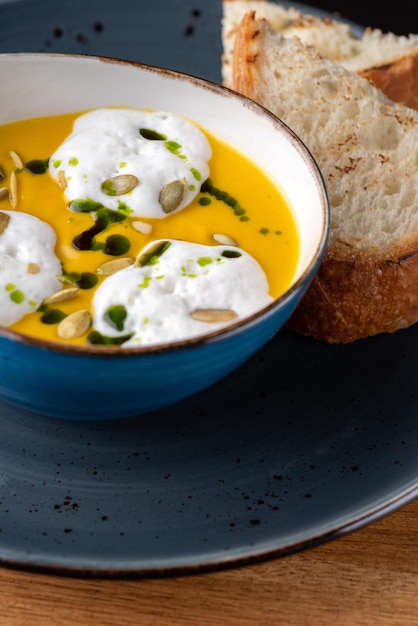 Zuppa di crema di zucca calda con spuma di cocco e pane su un tavolo di legno Cibo sano