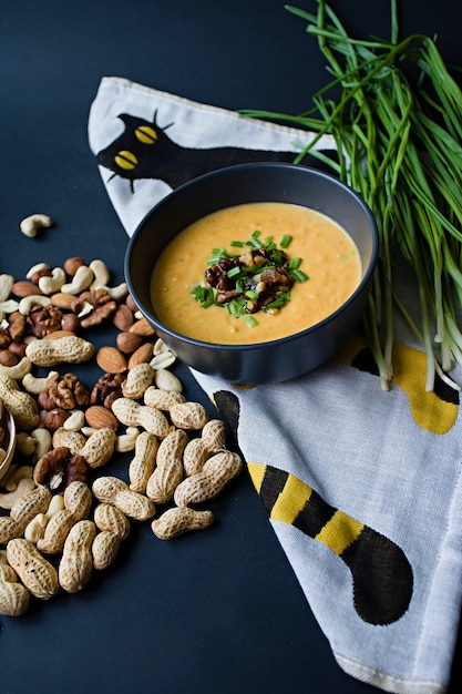 Zuppa di crema di zucca con erbe e noci, servita in una ciotola scura.