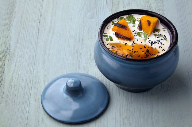 Zuppa di crema di zucca con panna, semi di cumino nero ed erbe aromatiche su un tavolo di legno azzurro