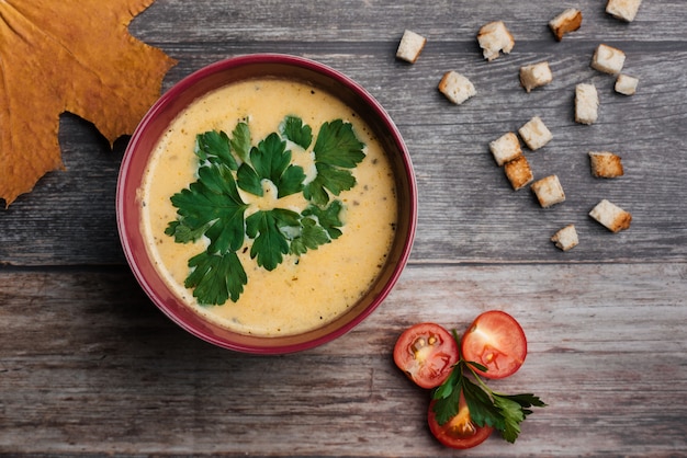 Zuppa di crema di zucca in una ciotola con prezzemolo sul tavolo di legno con cracker e pomodori. Tradizionale cibo autunnale per Halloween