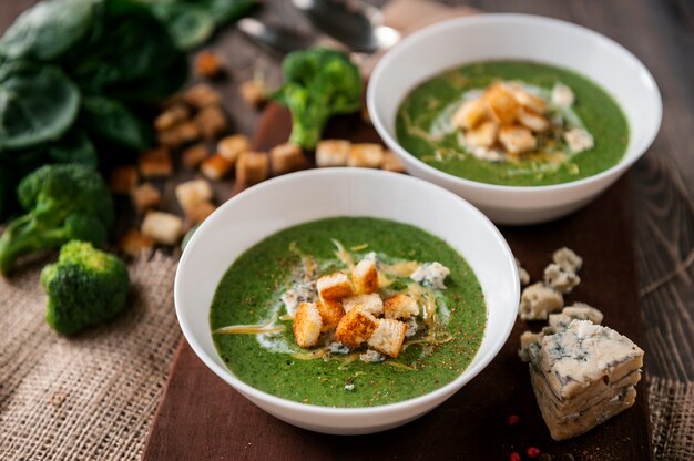 Zuppa di crema verde di spinaci e broccoli. con l'aggiunta di parmigiano e gorgonzola ai crostini. una superficie di legno.