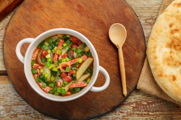 Zuppa di fagioli della cucina ebraica cholit su un supporto rotondo accanto al pane e un cucchiaio di legno orizzontale